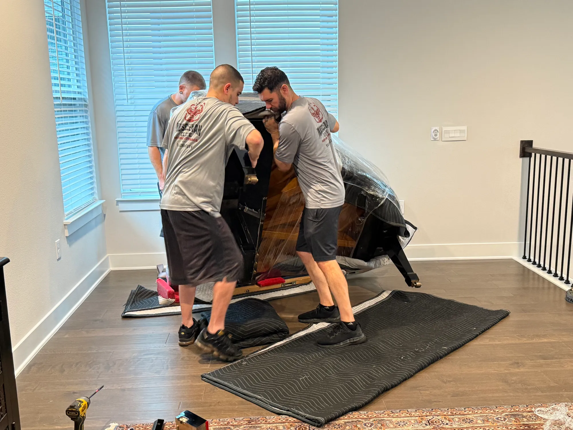 Muscleman Elite crew standing an upright piano back upright on moving blankets
