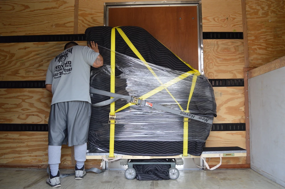 Muscle Man Moving employee safely securing a baby grand piano in the moving truck.
