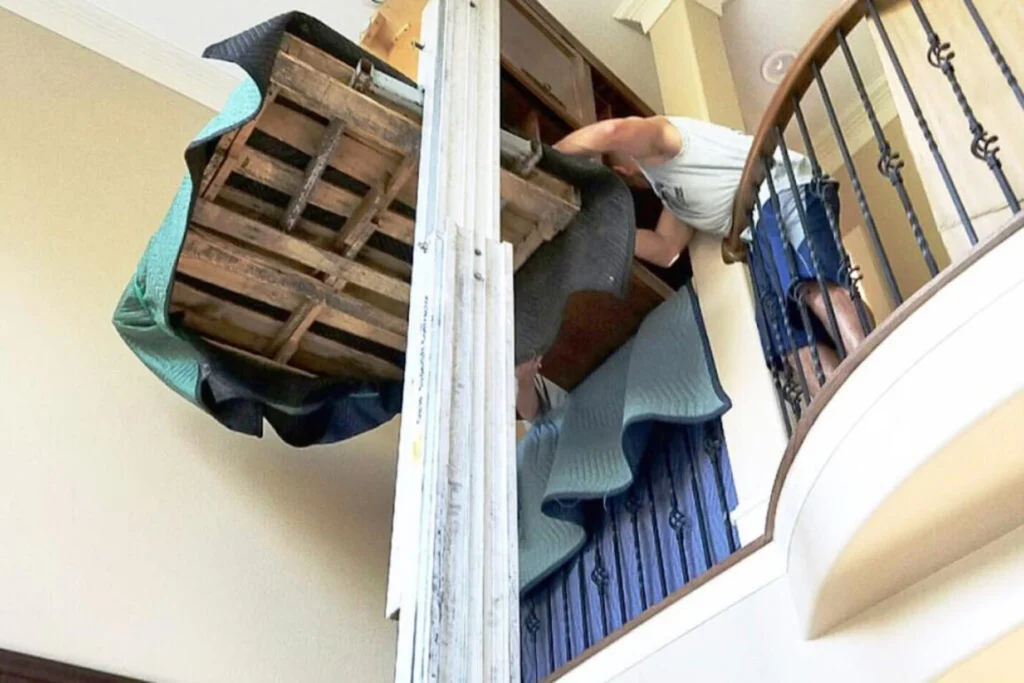 Long-distance piano movers using specialized equipment to lower a piano to the ground floor.
